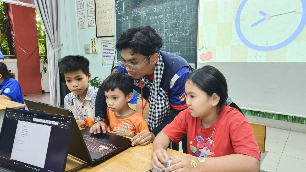 A YSS volunteer teaching a small group of children on a laptop during Misi Vietnam 2025